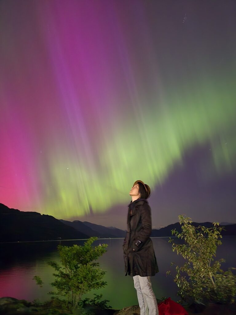 Artist Jenie Gao wearing a black jacket looking up at the aurora borealis.